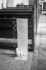 Memorial plaque with inscriptions on a church pew, with candles placed in front.